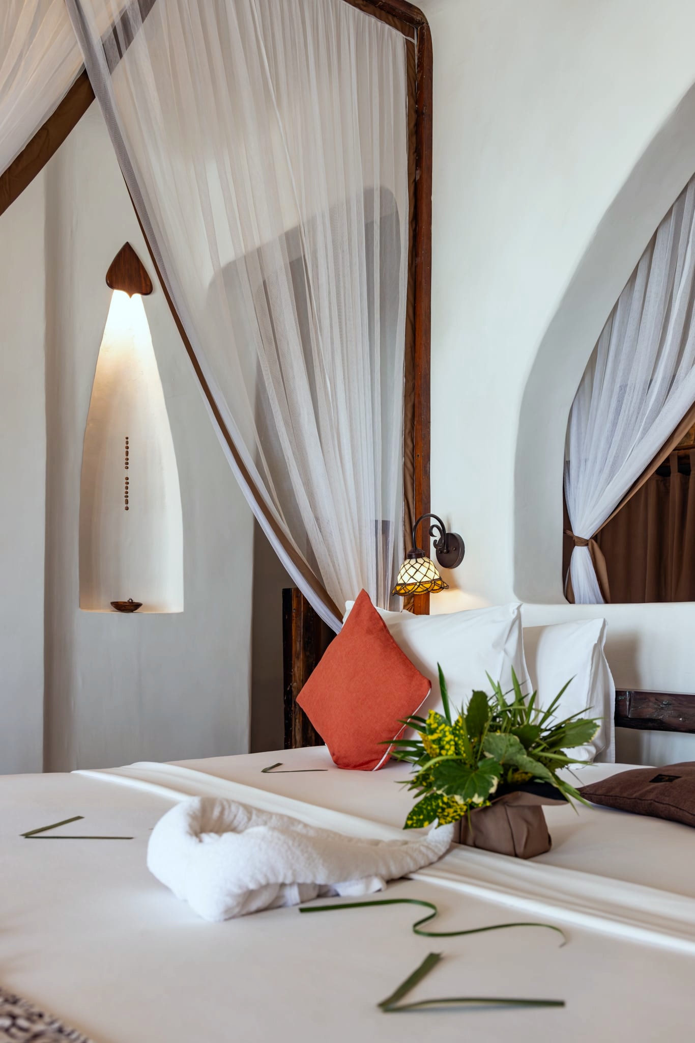 Dunia: a bed under a mosquito net against white walls, flowers laid across the linen.