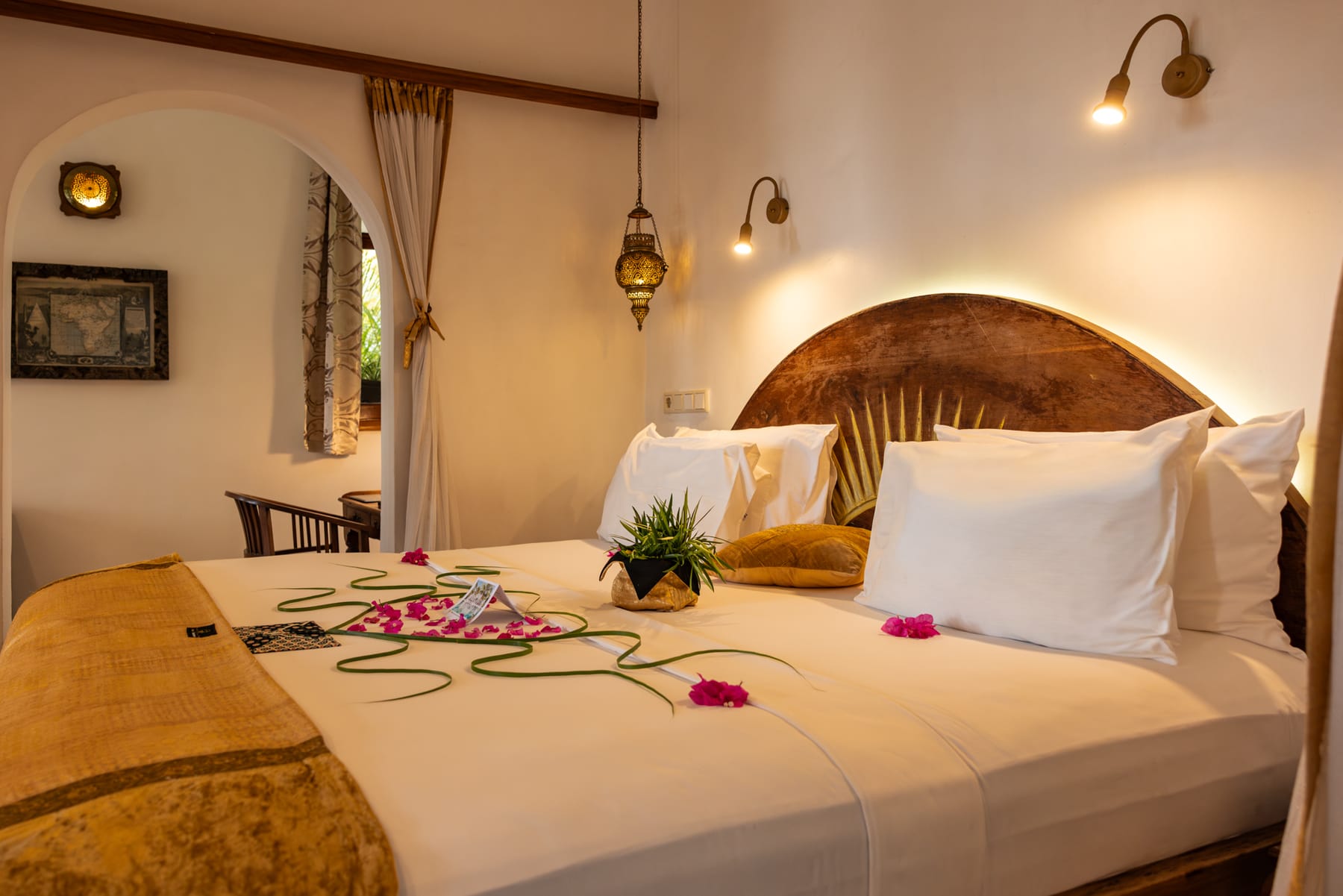 La cama de la suite Jua de Villa Kidosho, con ropa de cama blanca y pétalos de flores, bajo un cabecero de madera tallada.