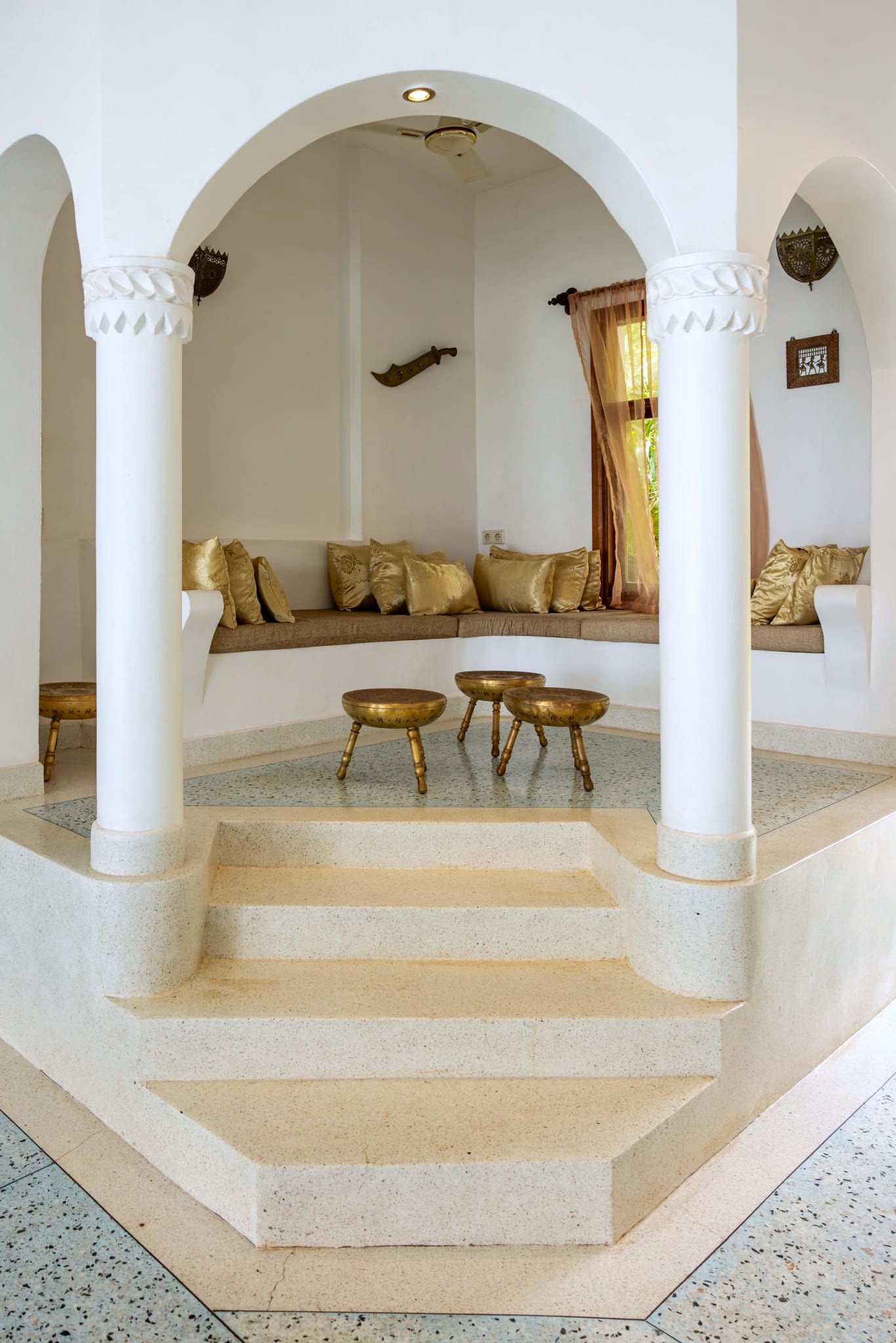 Les banquettes baraza de la Villa Kidosho : bancs maçonnés, coussins dorés, tabourets en laiton.