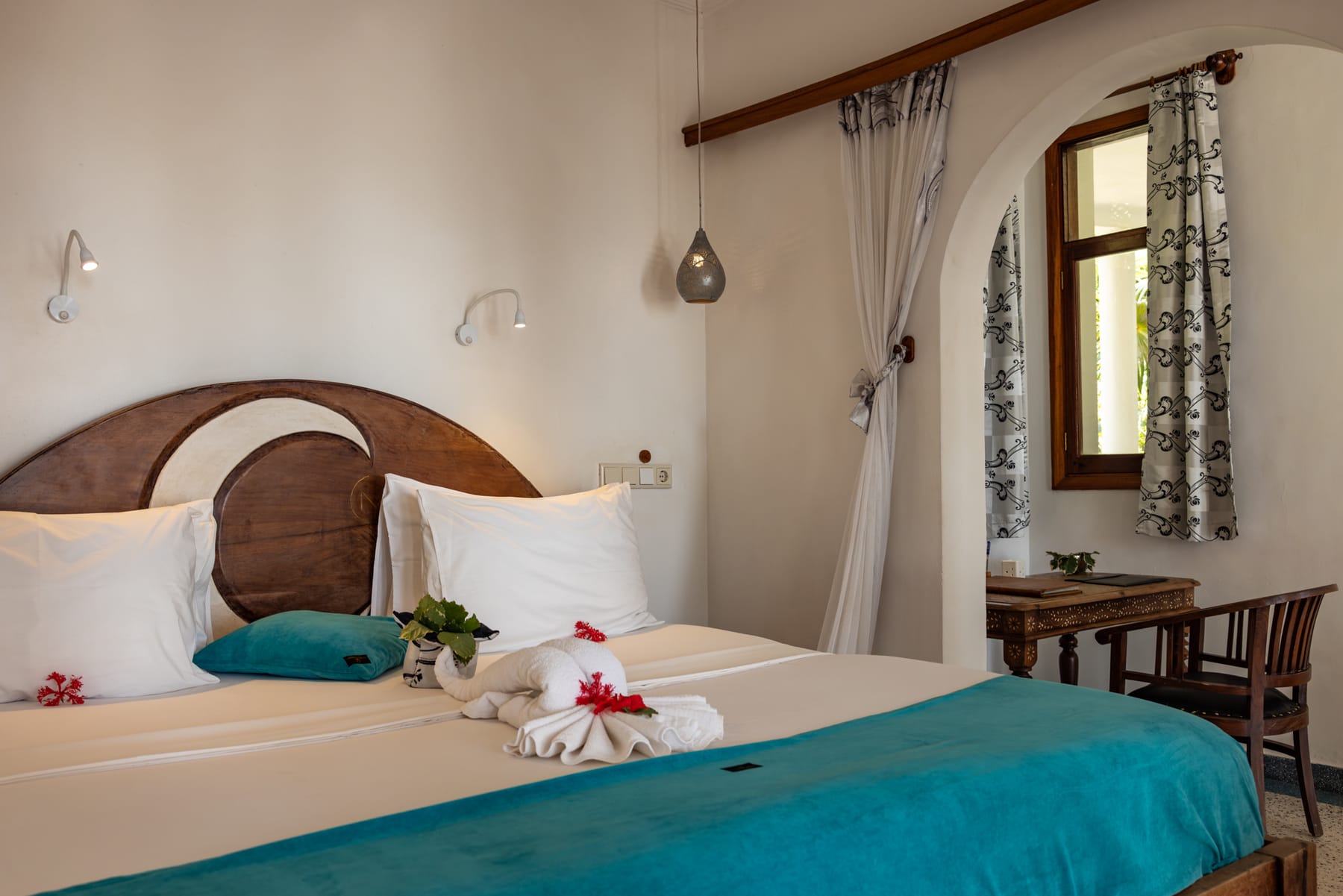 La cama de la suite Mwezi de Villa Kidosho, con cabecero de madera tallada, colcha turquesa y una toalla doblada.