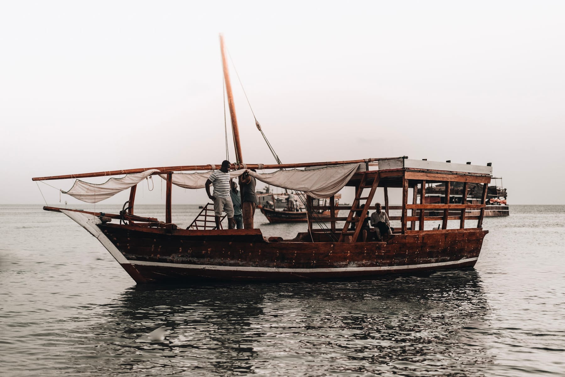 Traditional wooden dhow sailing on calm water in Zanzibar with people aboard