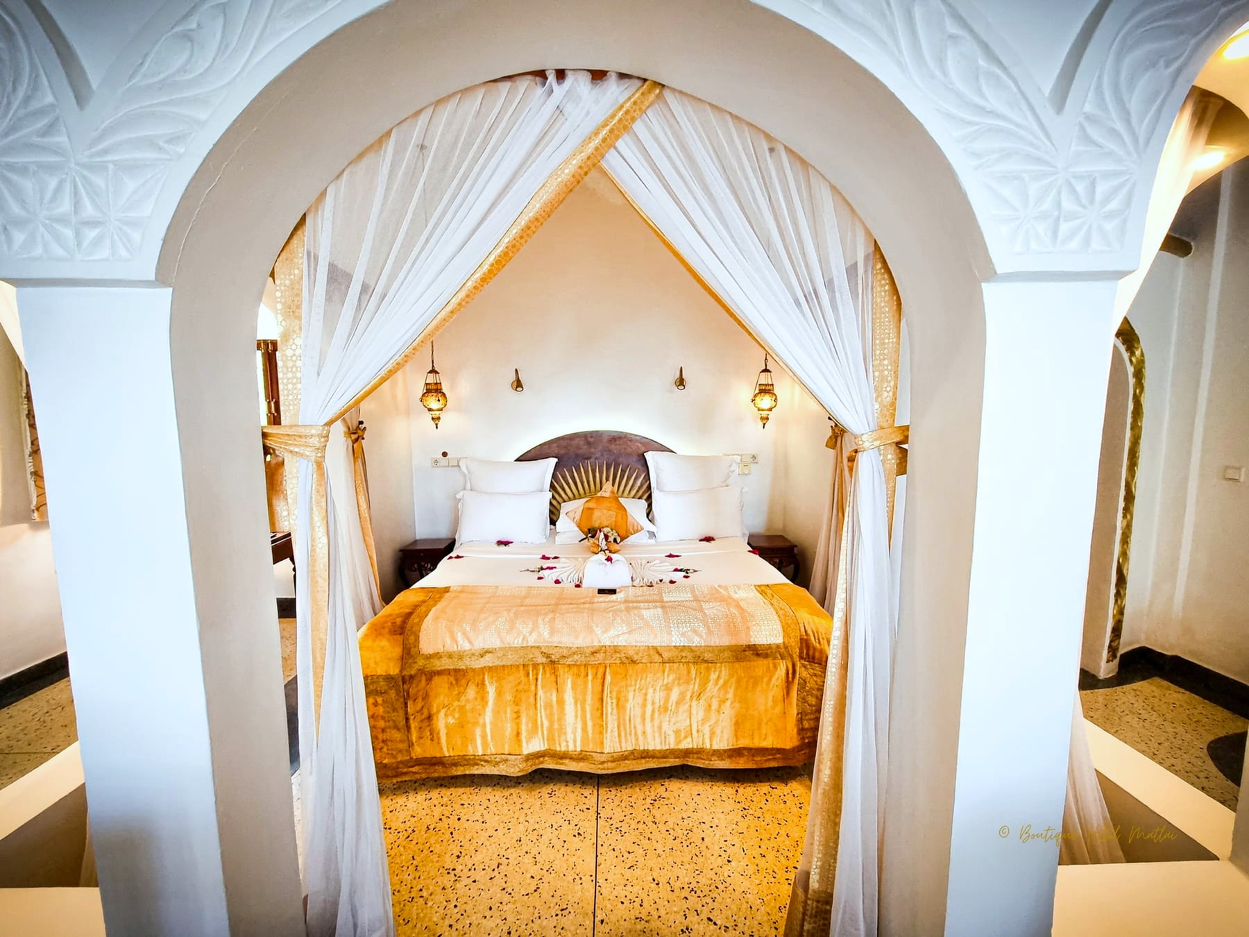 Una suite di Villa Kidosho: un letto con copriletto dorato e tende bianche, incorniciato da un arco intagliato