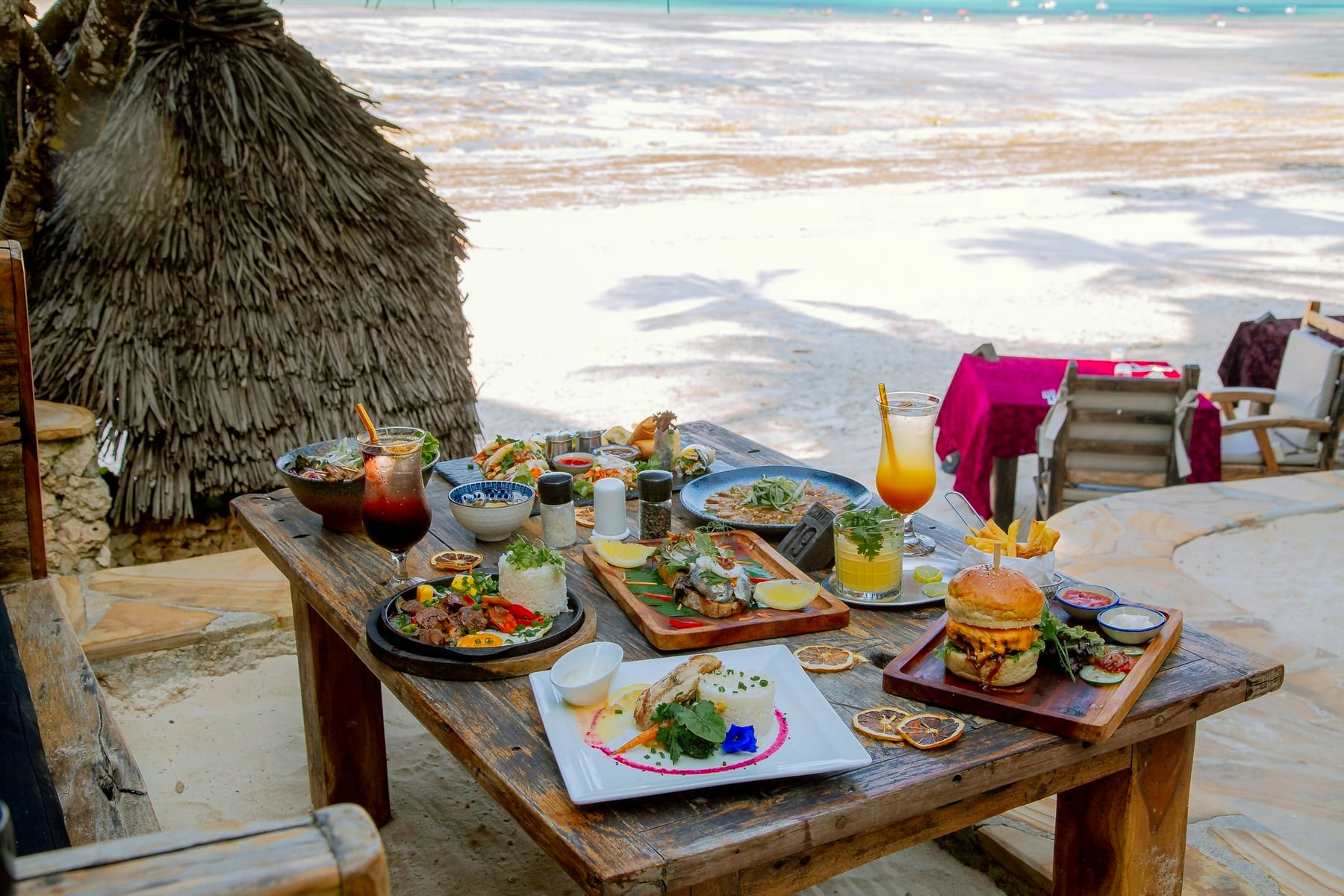 Una mesa con platos servidos sobre la arena, frente al mar, en el restaurante Zatiny