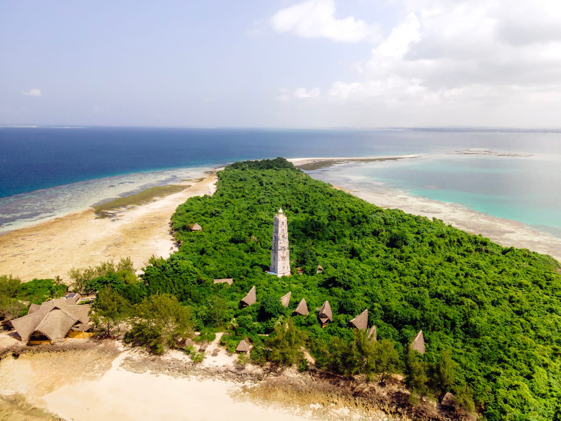A small green island with a lighthouse and pale beaches, seen from above