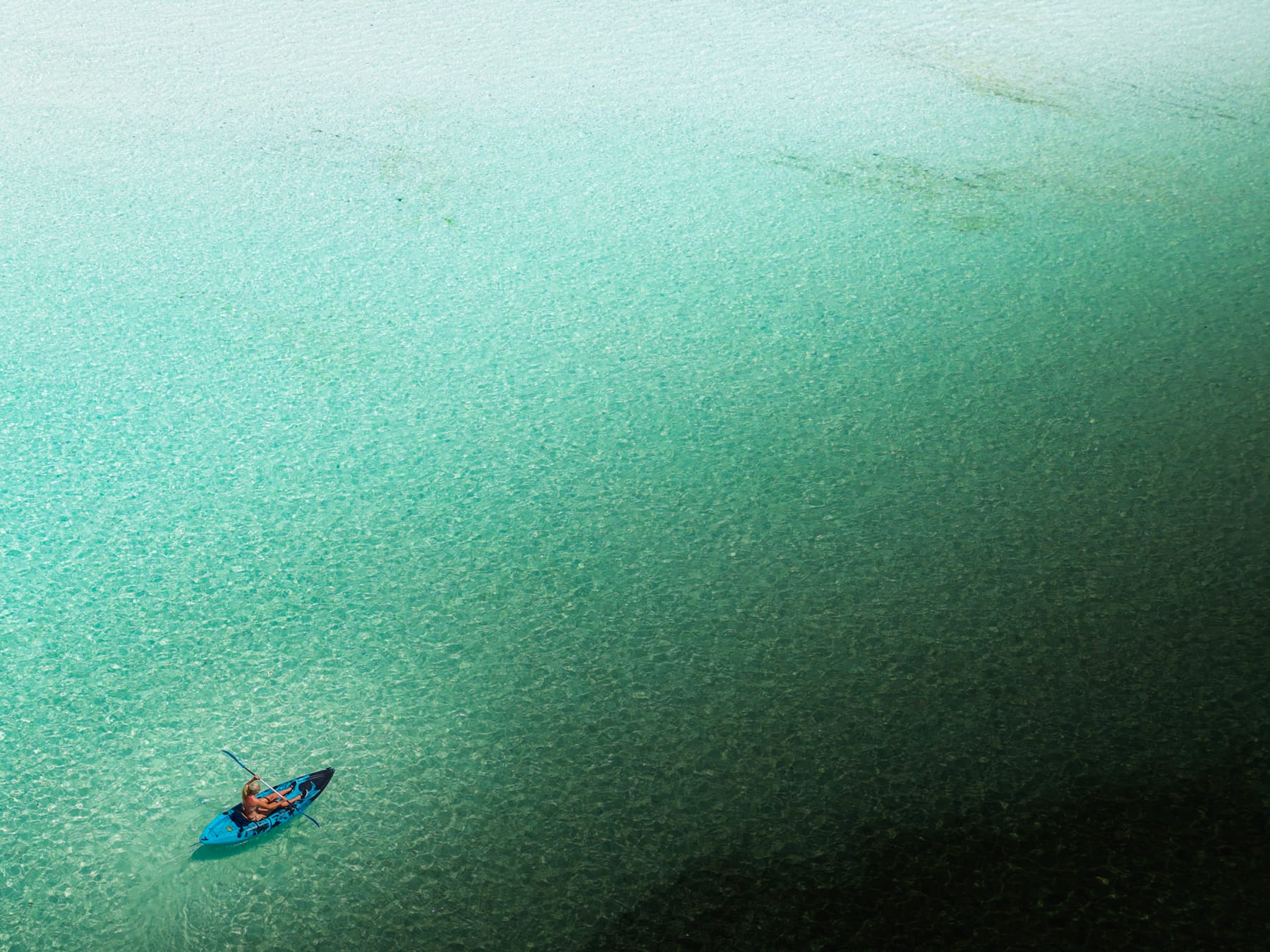 A single kayaker on clear turquoise water, seen from above