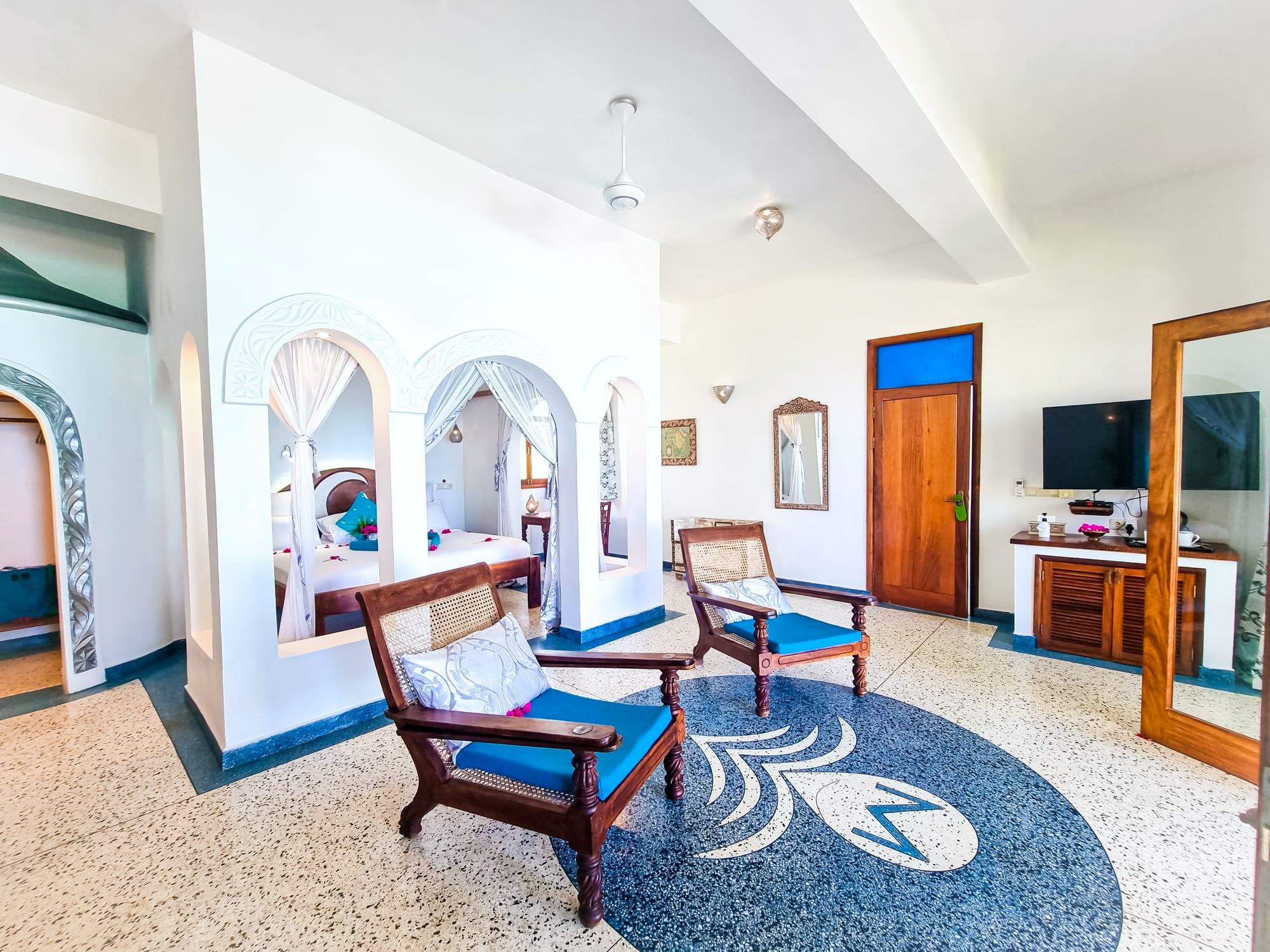 The Mwezi suite at Villa Kidosho, blue-cushioned planter chairs and the arched alcove over the bed