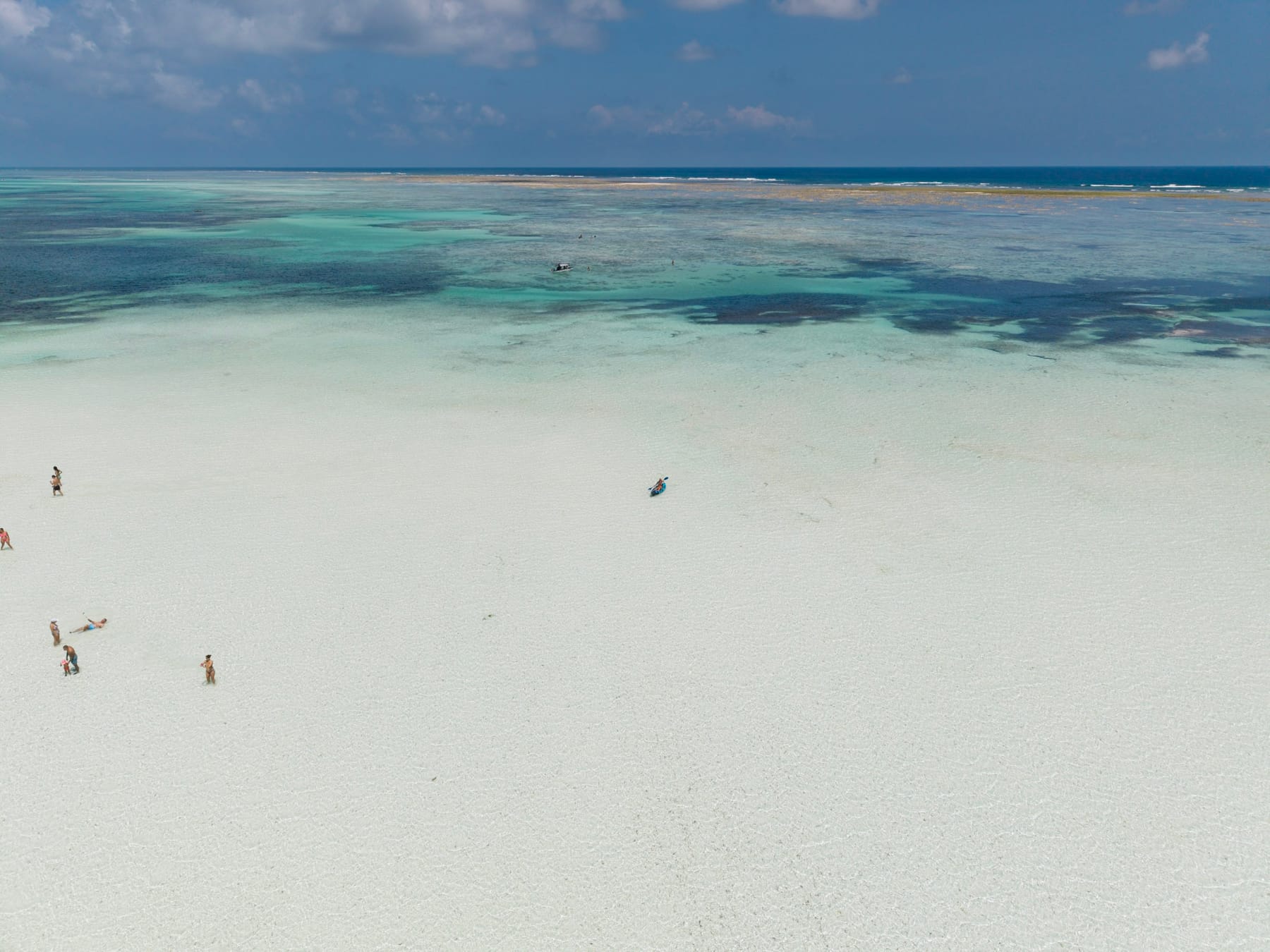 Zanzibar's east coast at low tide from the air: shallow turquoise water over the reef flat, a few people walking far out