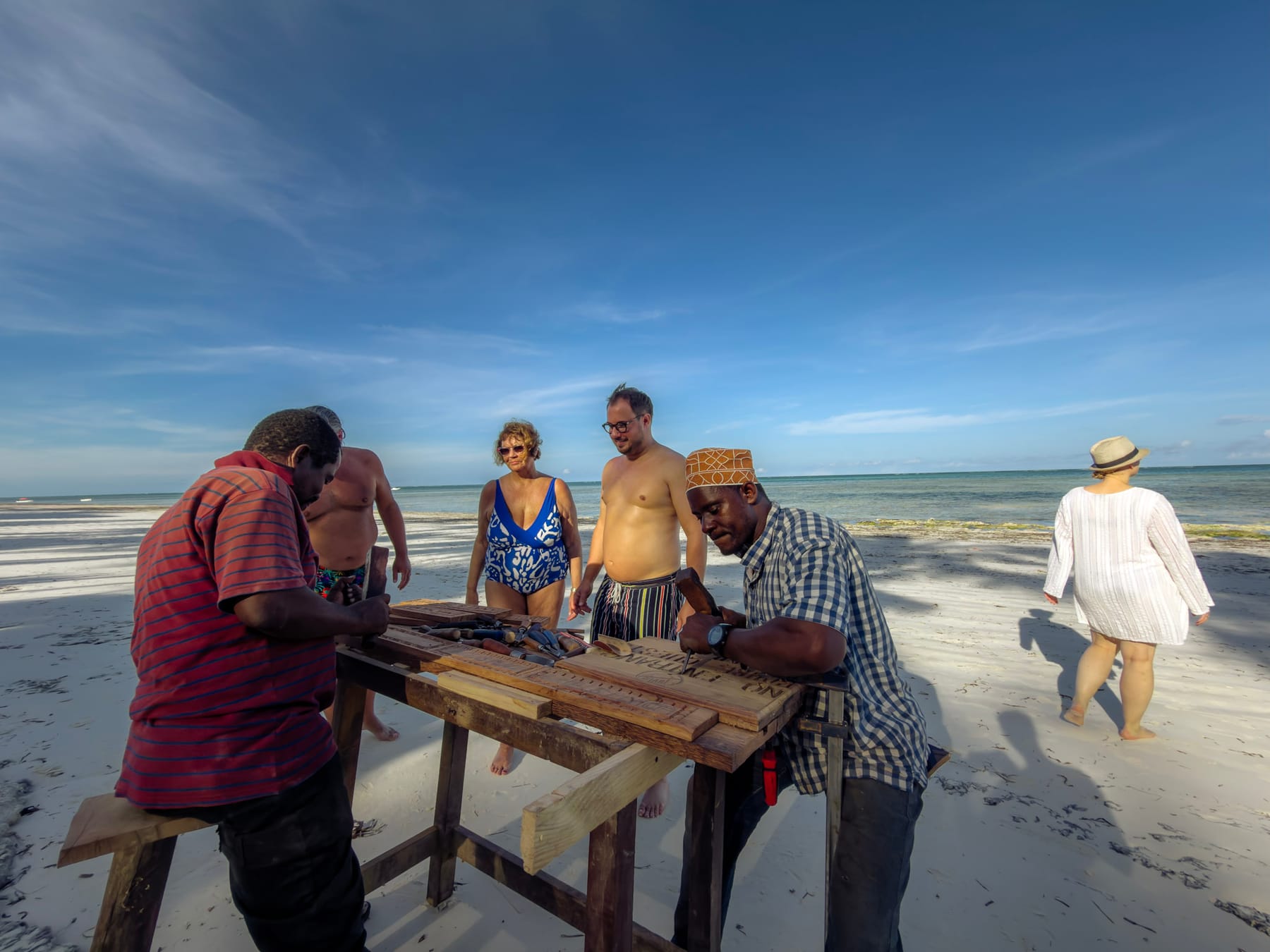 Kunsthandwerker schnitzt Holz an einem Strand auf Sansibar, während Besucher zusehen