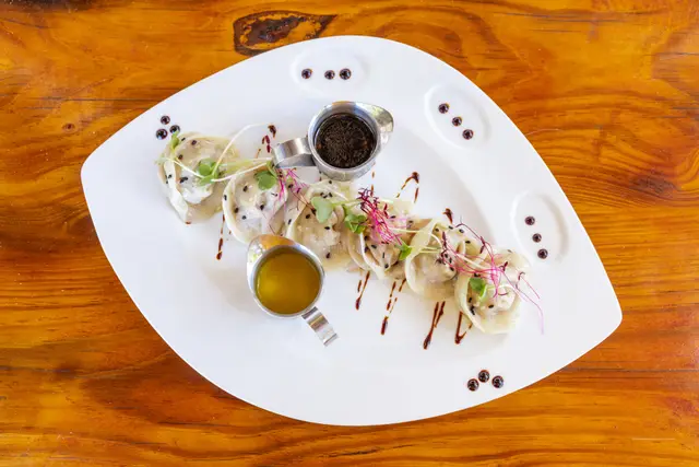 Dumplings with two dipping sauces on a white plate on a teak table, seen from above
