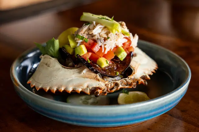A crab dish with diced vegetables served in a crab shell on a blue-rimmed bowl