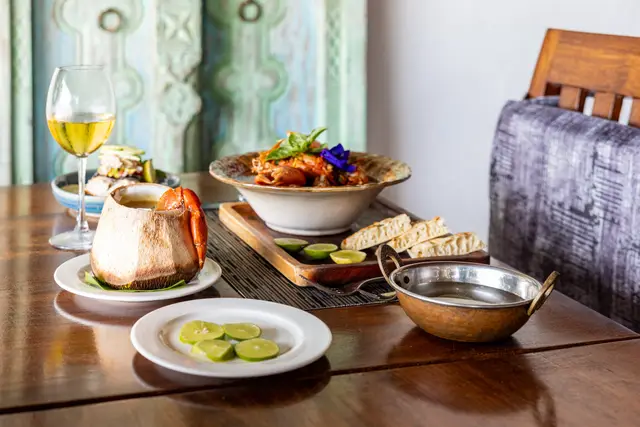 A wooden table at Zatiny set with a crab dish, bread, a bowl of guacamole and two glasses of white wine, in front of a carved turquoise door