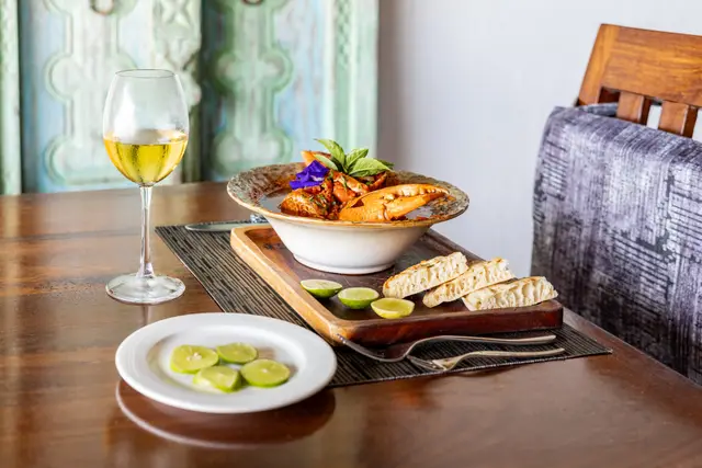 A crab dish in a bowl beside a glass of white wine and a small side plate on a wooden table