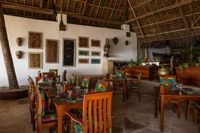 The thatched dining room of Zatiny, with wooden tables, orange chairs and framed pictures on the wall