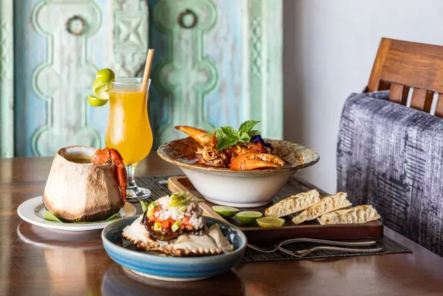 A restaurant table set with a fruit drink and two dishes in front of a carved turquoise door