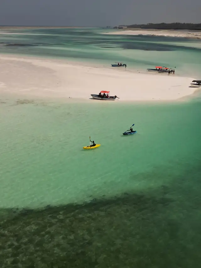 Two kayaks on turquoise water beside a pale sandbank, seen from above