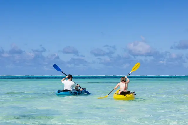 Two kayaks paddling across clear turquoise shallow water under a blue sky