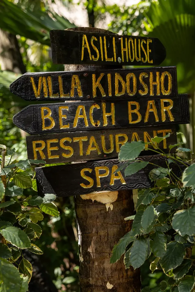 A wooden signpost in the garden pointing to Asili House, Villa Kidosho, the beach bar, the restaurant and the spa