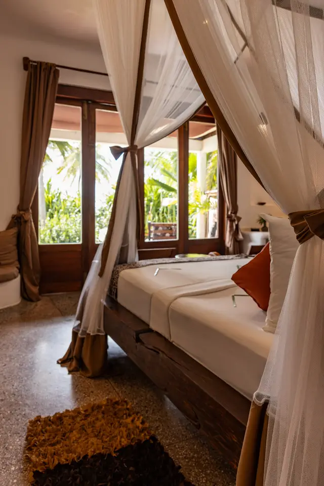 The bed in the Dunia room under a mosquito net, with the balcony doors and a palm tree beyond