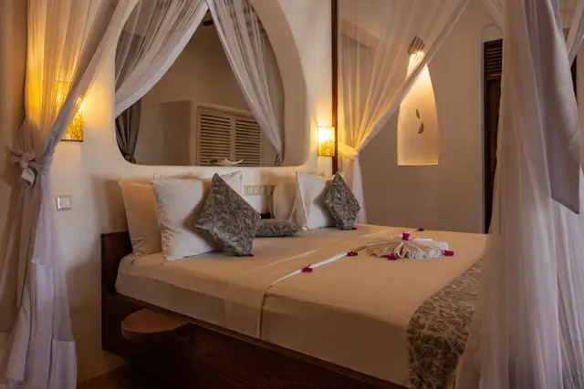 Bed under a white mosquito net, with flowers laid on the linen, in the Hewa room at Asili House