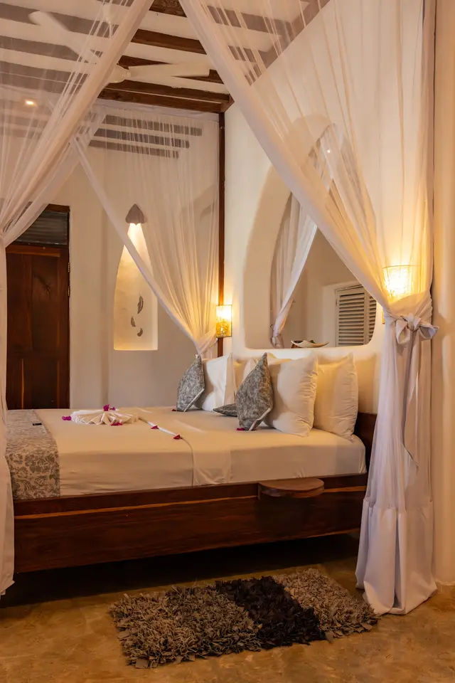 The Hewa bedroom in warm evening light: a bed with a canopy and a carved niche in the wall