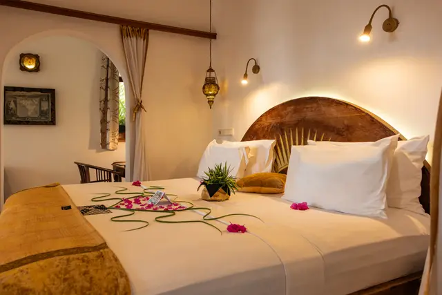 A bed in the Jua suite with petals laid across it and a carved headboard in an arched alcove