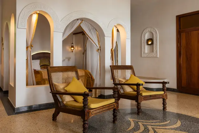 The sitting area of the Jua suite with two wooden chairs and yellow cushions between arched alcoves