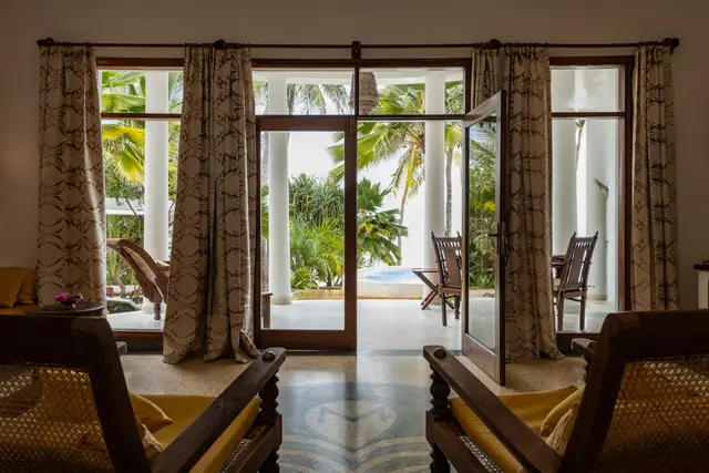 Wooden armchairs in the Jua suite, with tall glass doors opening to the garden and the pool beyond