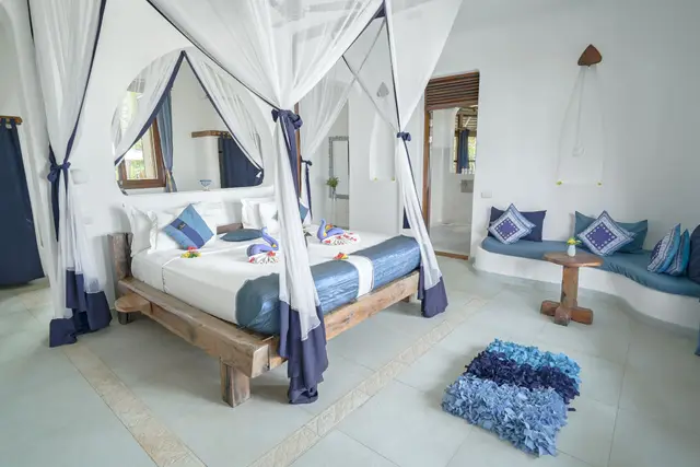 The Maji bedroom: a canopy bed with blue accents and towel swans, a built-in seat with blue cushions and a blue rug