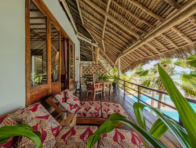 The thatched balcony of the Moto room with kanga-print daybeds, palm leaves in the foreground and the pool below