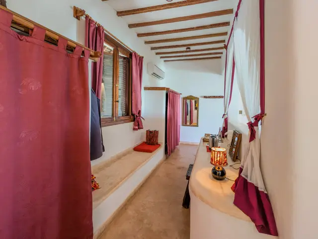 The dressing nook of the Moto room with red curtains, a built-in cushioned bench along the wall and a table lamp