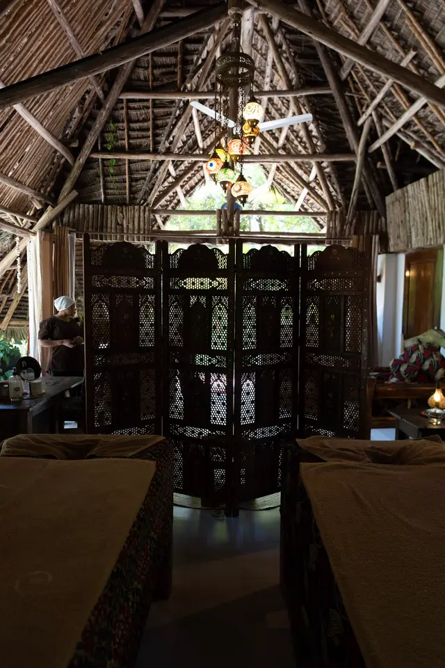 Two treatment beds under a high thatched roof, with carved wooden screens at the far end